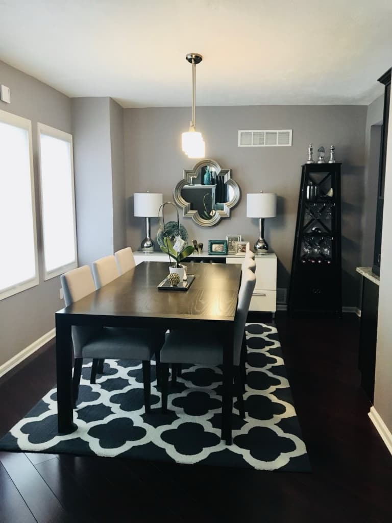 Open dining room with a dark wood table, upholstered chairs, pendant light, and patterned rug after renovation