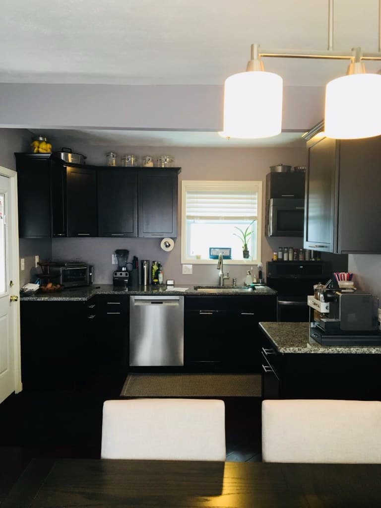 Rebuilt kitchen seen from the dining area with dark cabinets, granite, and pendant lighting after renovation