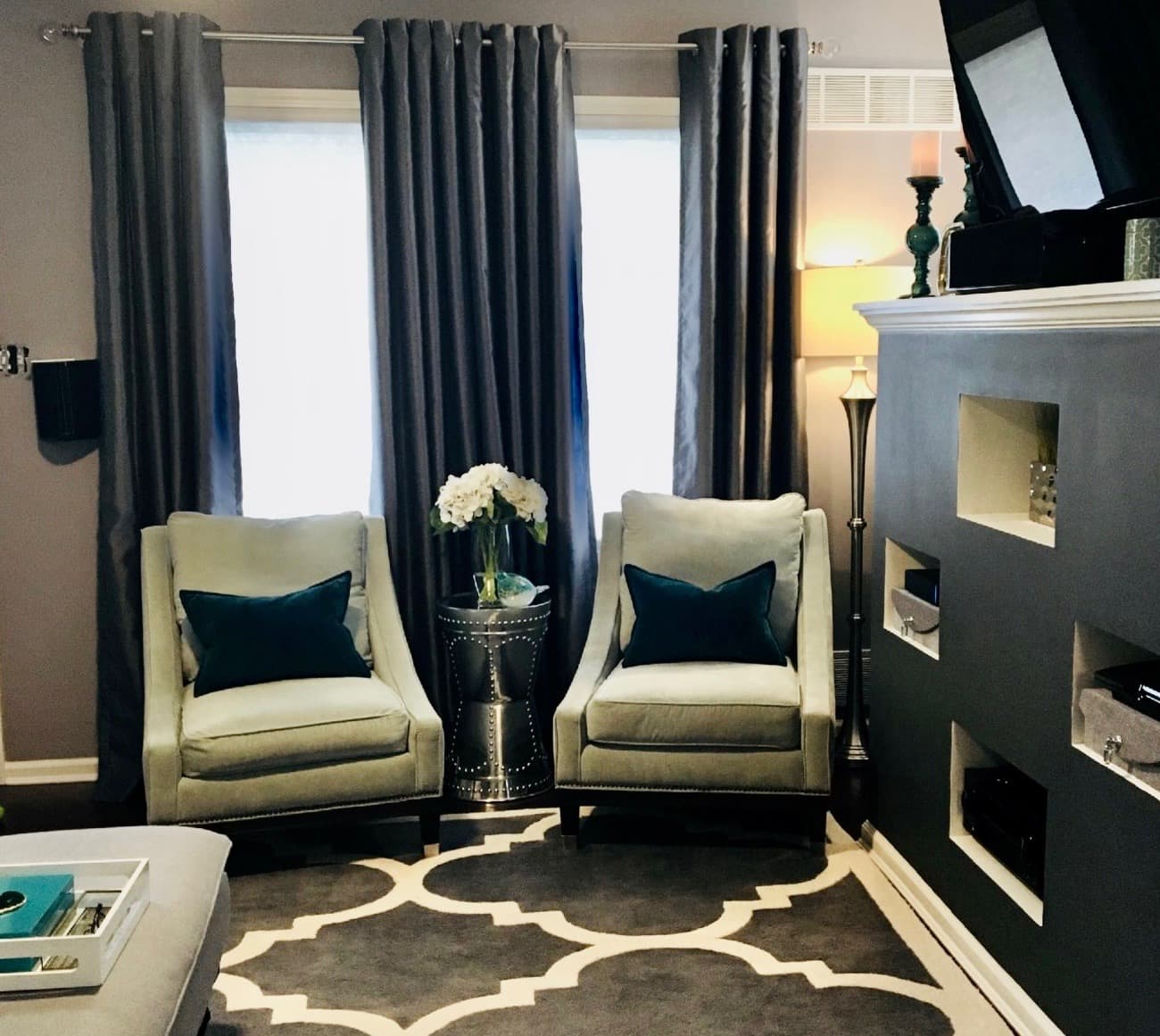 Refined sitting area with two cream accent chairs, floor-length drapes, and a patterned rug after renovation