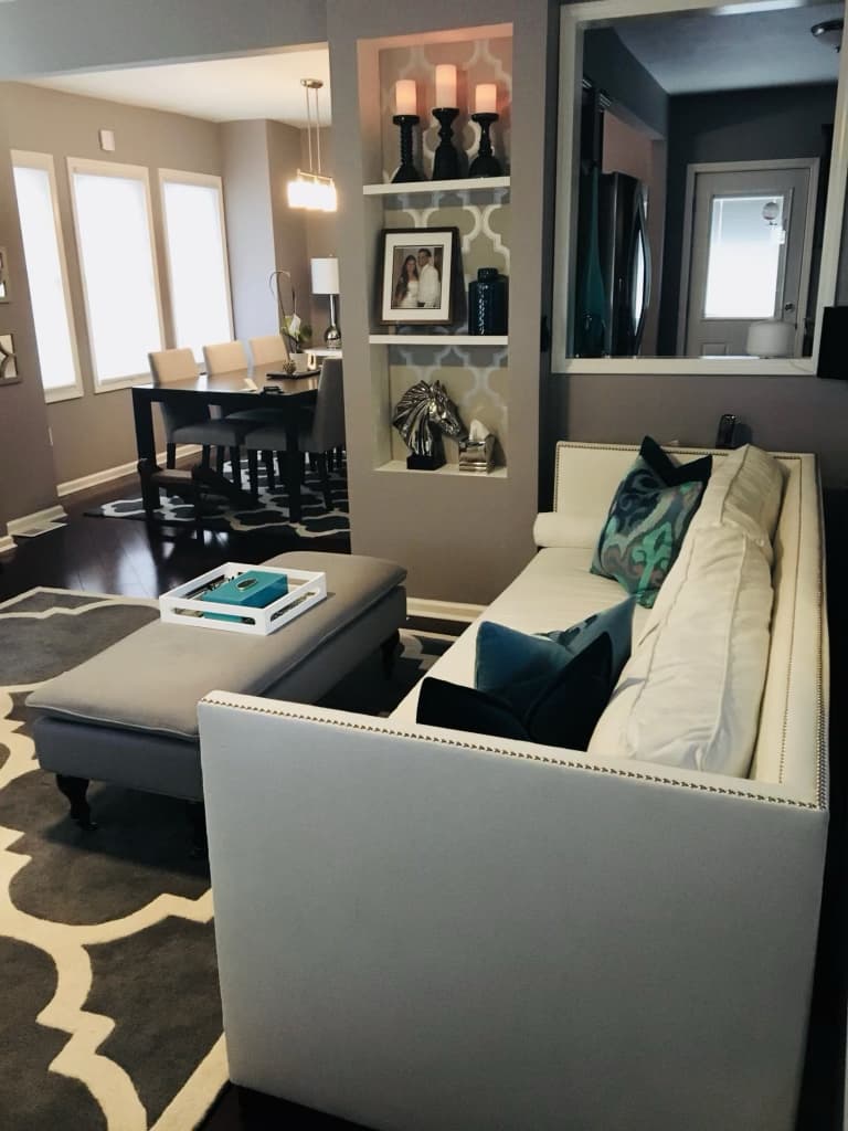 Open-concept living area with a cream sofa, ottoman, and a lit built-in niche