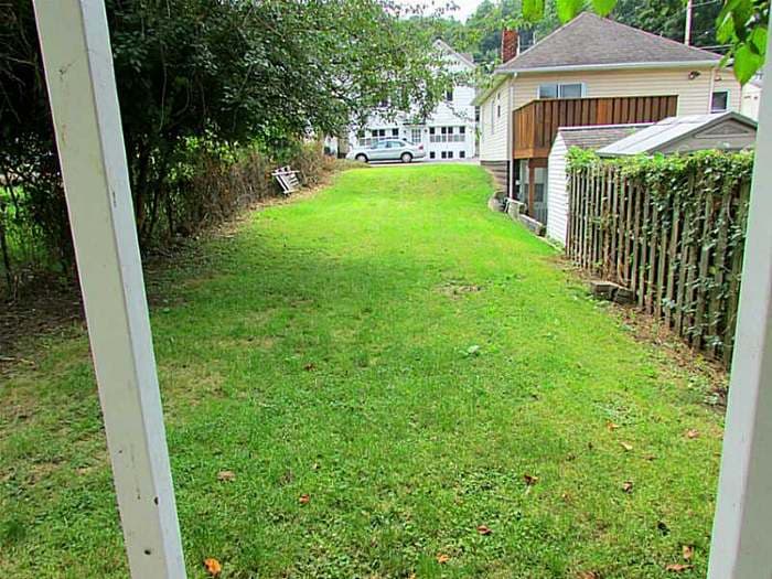 Narrow sloped backyard with patchy grass and fencing before renovation