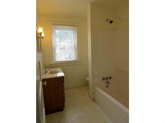 Dated bathroom with an oak vanity, old tub, and worn floor before renovation