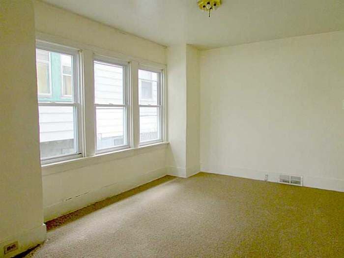 Empty bedroom with three windows and beige carpet before renovation