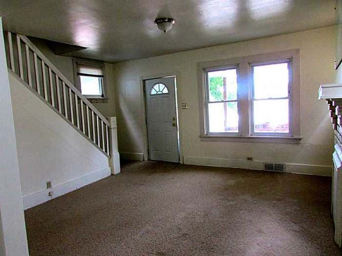 Front room with a white-banister staircase, front door, two windows, and worn carpet before renovation