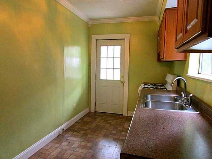 Dated kitchen with green walls, wood cabinets, and an old rear door before renovation