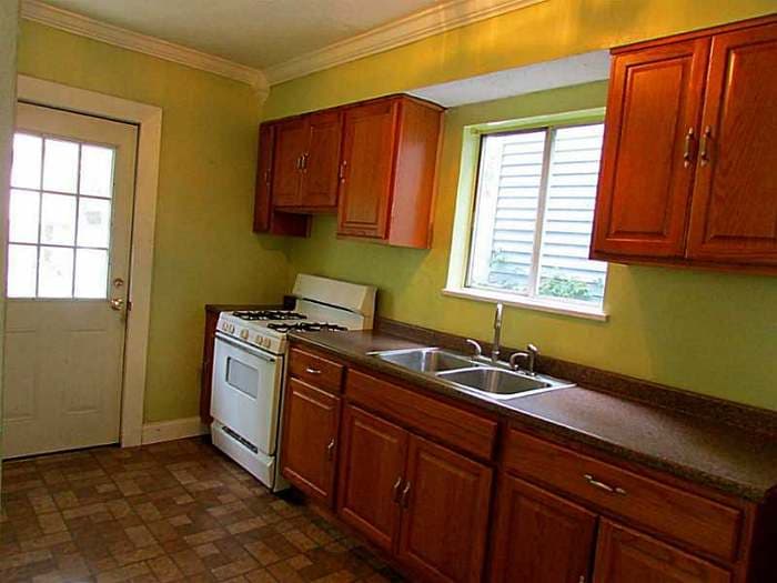 Dated kitchen with green walls, wood cabinets, a gas range, and a checkerboard floor before renovation