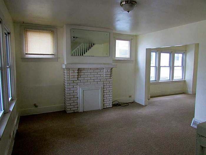 Living room with a brick fireplace, overhead mirror, and bay window before renovation