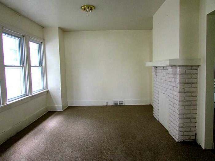 Living room with a white painted brick fireplace and dark carpet before renovation
