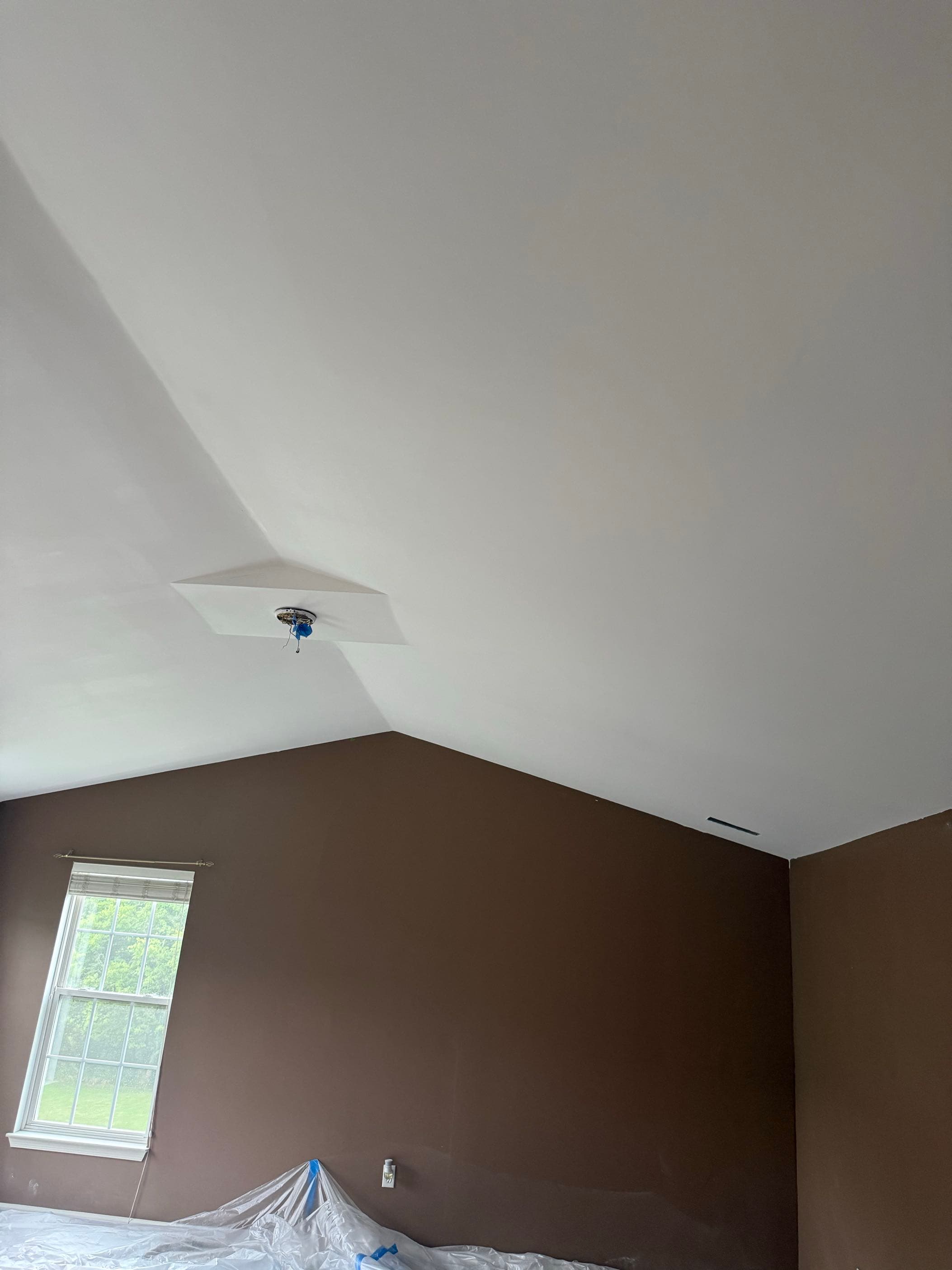 Smoothed and painted vaulted, angled ceiling meeting brown accent walls in a bedroom