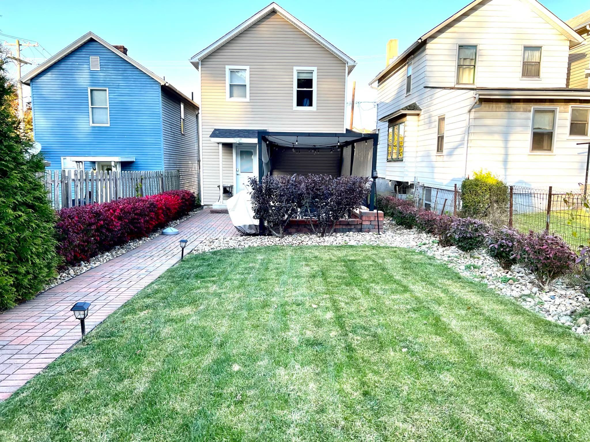 Landscaped backyard with fresh sod, a paver walkway, and a pergola-covered patio after renovation