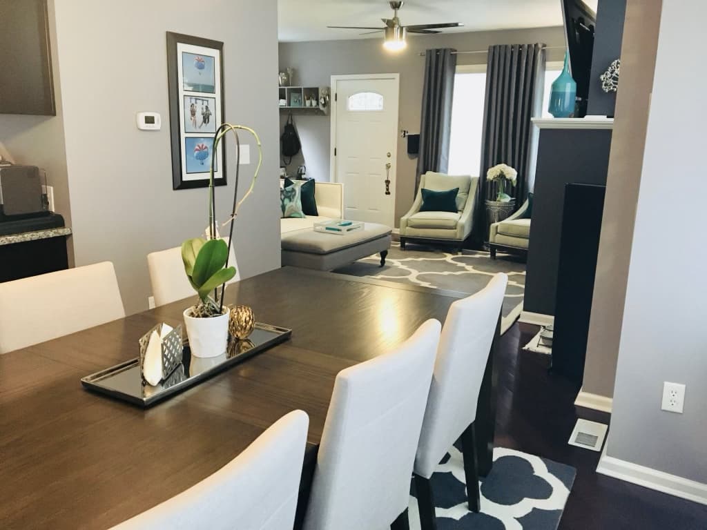 Same front room after renovation, seen from the dining table, with new flooring, drapes, and furnished living area