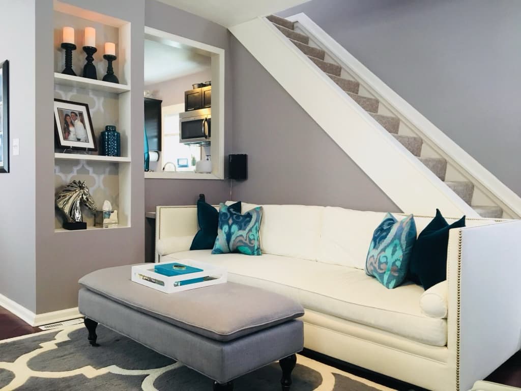 Living room with a cream nailhead sofa beside a freshly carpeted staircase after renovation