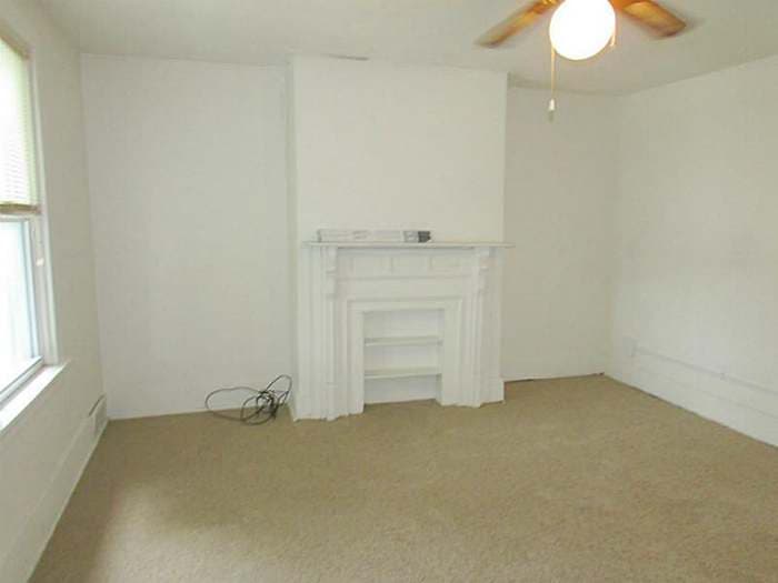 Living room with a white wood fireplace mantel and beige carpet before renovation