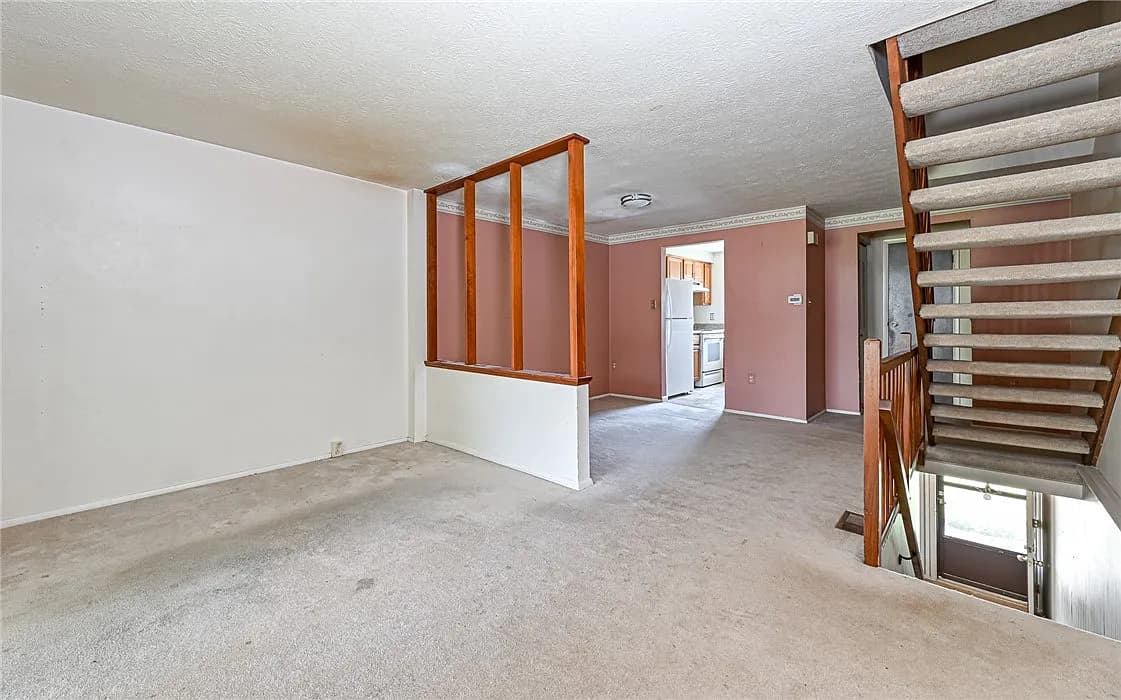 Living room before remodel with old carpet, pink walls, and a spindle half-wall dividing the space