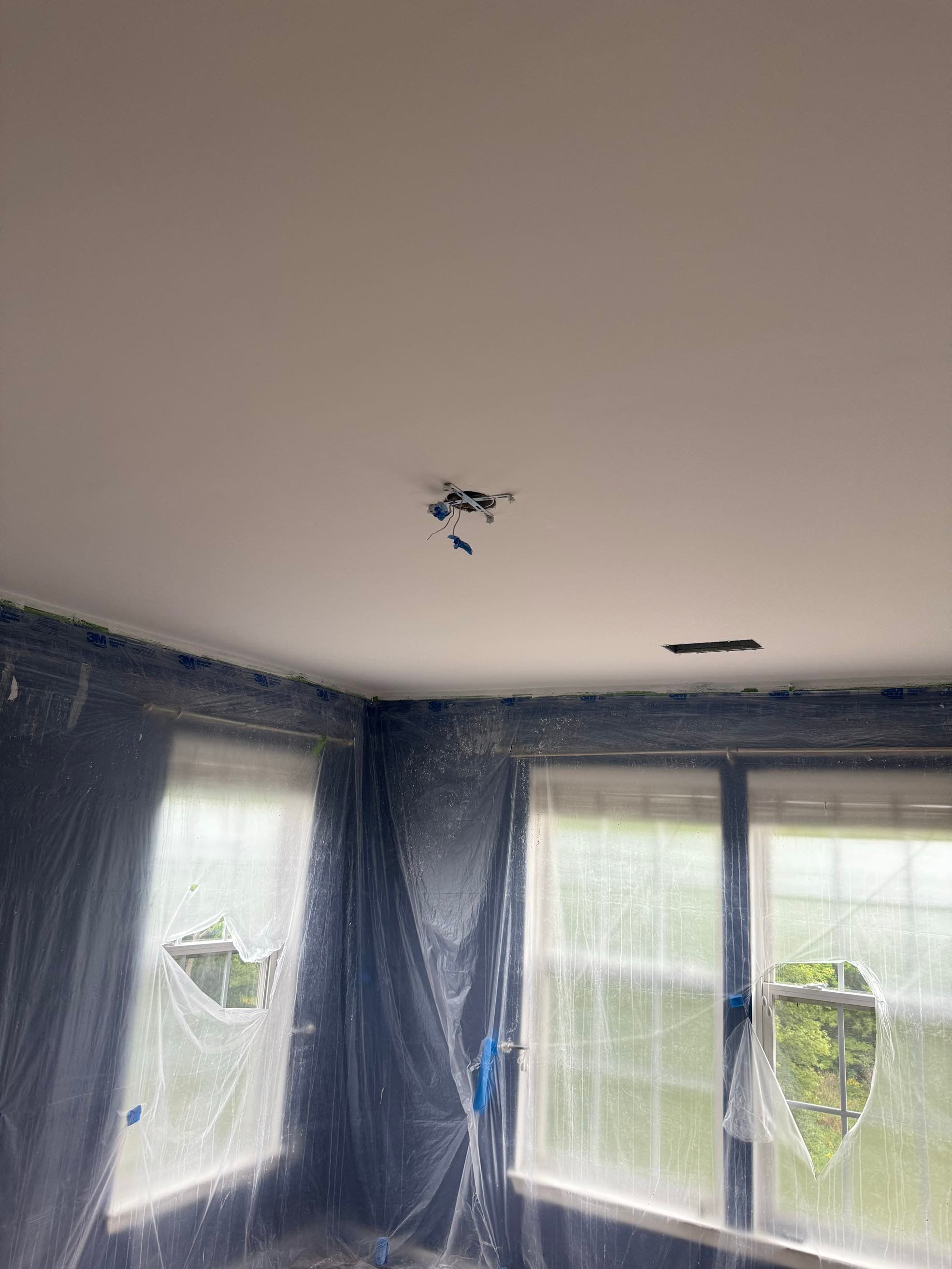 Bedroom with windows masked in plastic and a freshly smoothed, painted ceiling above