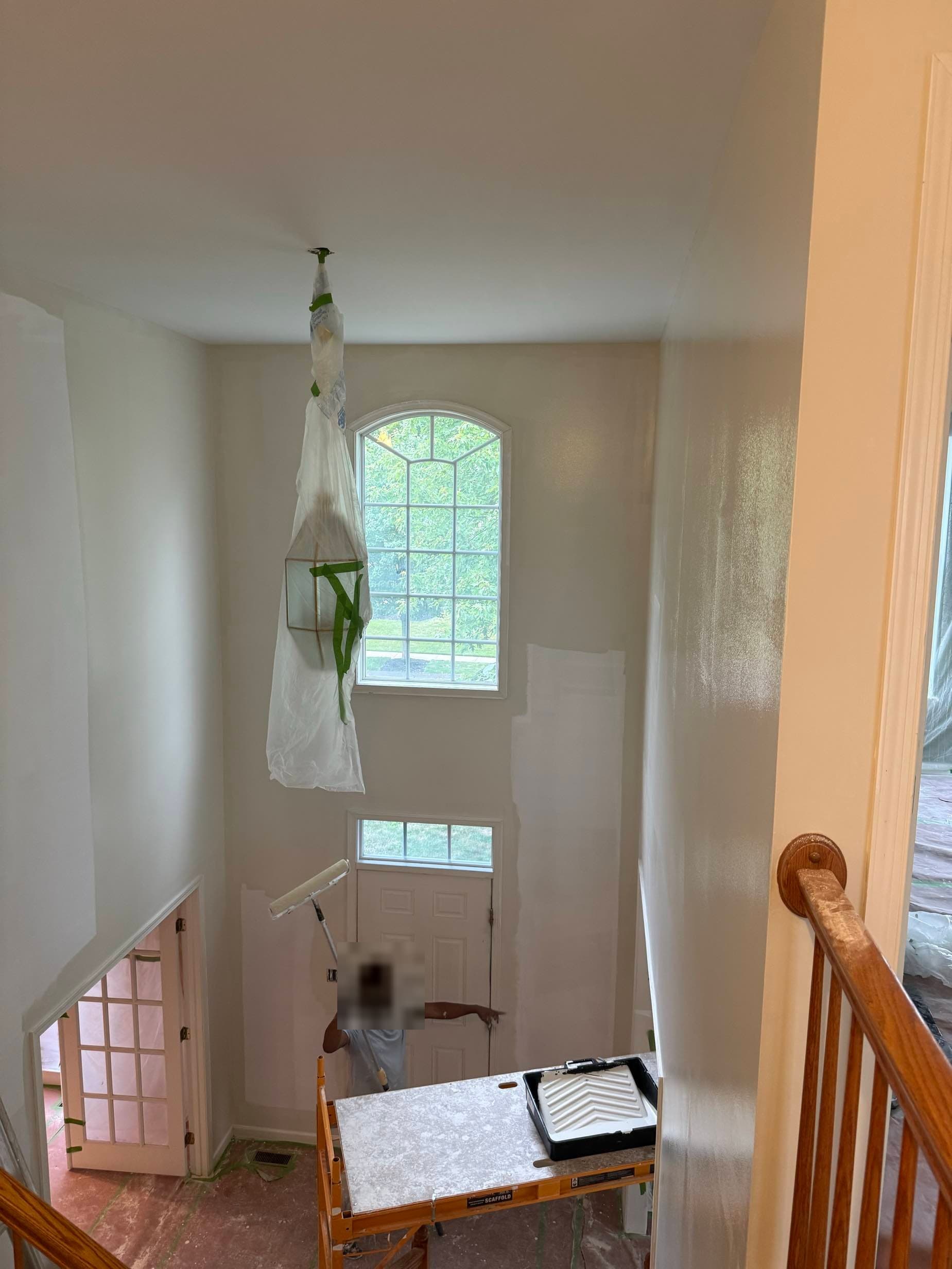 Worker on a scaffold rolling a smoothed, freshly painted two-story foyer ceiling beneath an arched window
