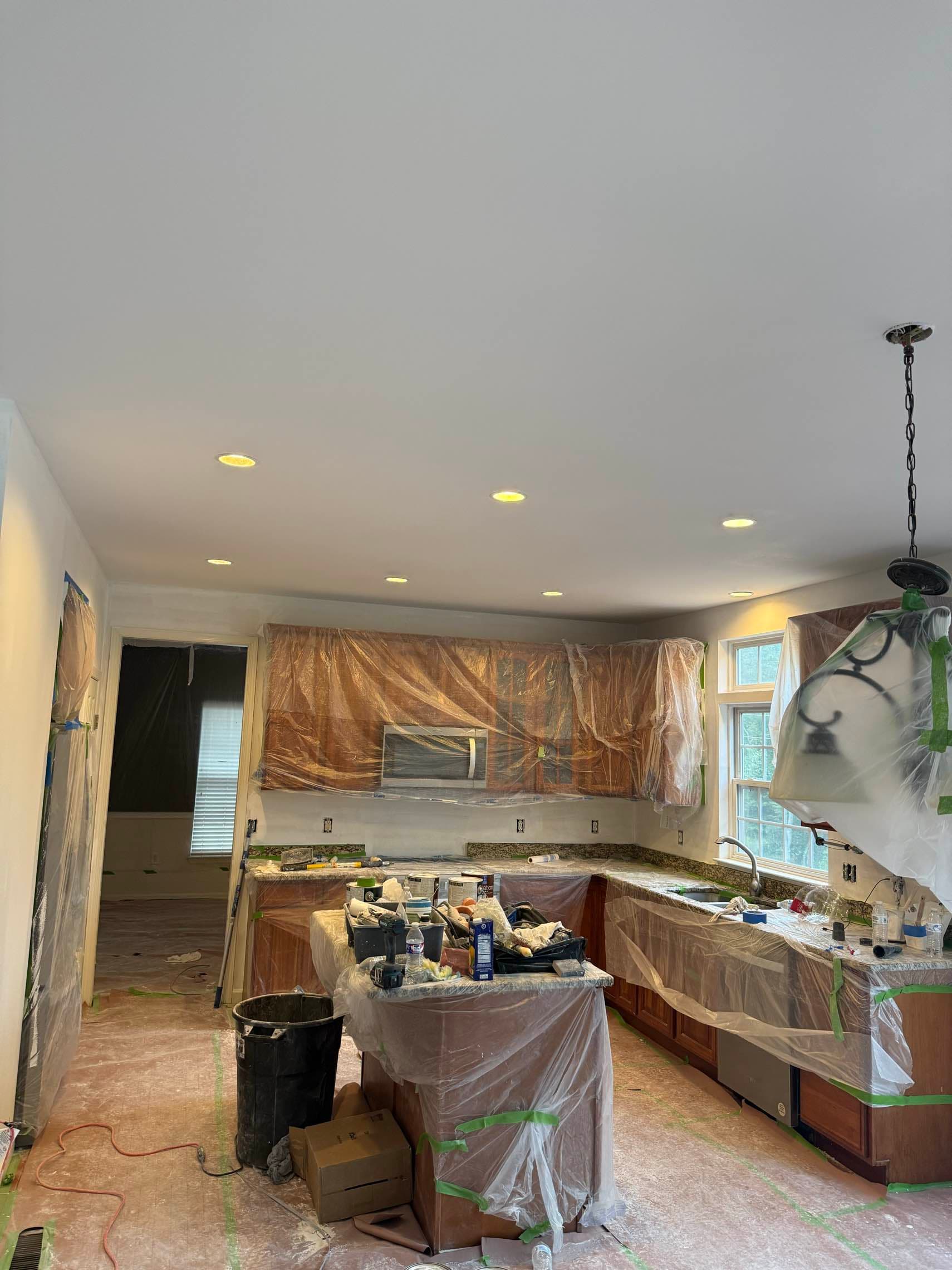 A freshly smoothed and painted kitchen ceiling with recessed lighting and cabinets carefully covered
